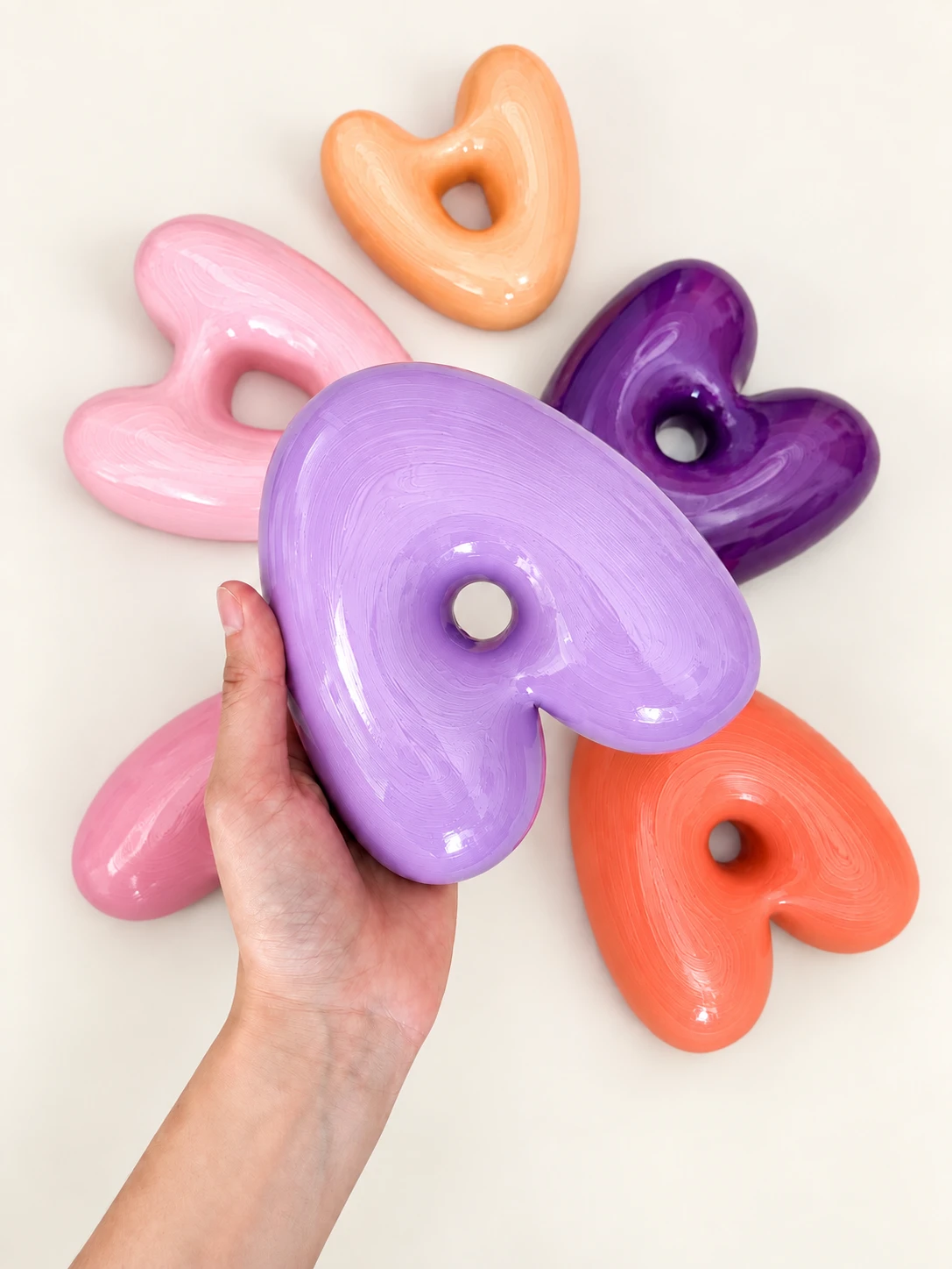 Mano sosteniendo una figura de corazón, rodeada de otros corazones de colores